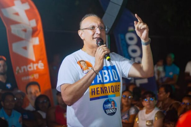 Fábio Henrique discursa ao microfone durante comício noturno, com bandeiras de campanha ao fundo