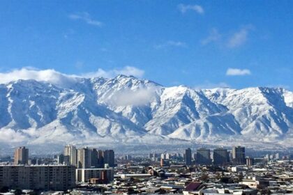 Vista da cidade de Santiago, no Chile, com prédios em primeiro plano e a Cordilheira dos Andes coberta de neve ao fundo, sob céu azul